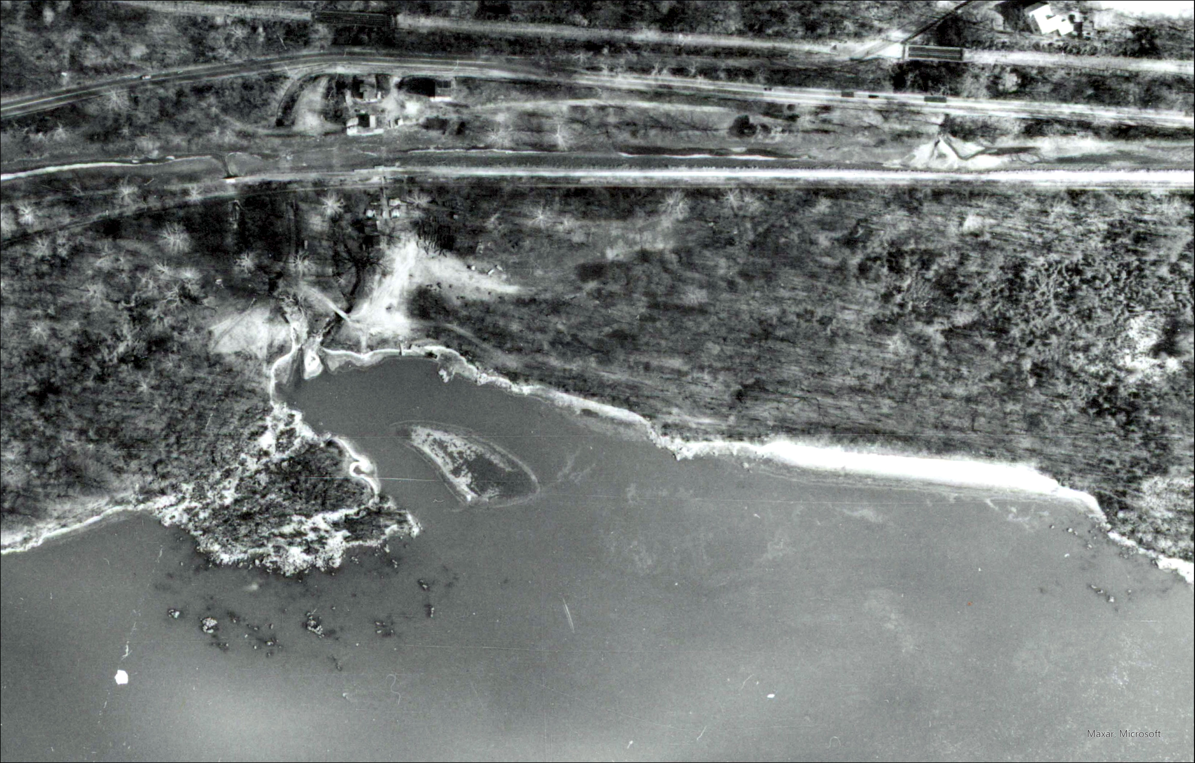 Black and white aerial photo of Fletcher’s Cove that shows a wide worn area in place of the previous dirt path from the boathouse to the Potomac River.  The Potomac River is at the bottom of the image and the Chesapeake and Ohio Canal is towards the top.