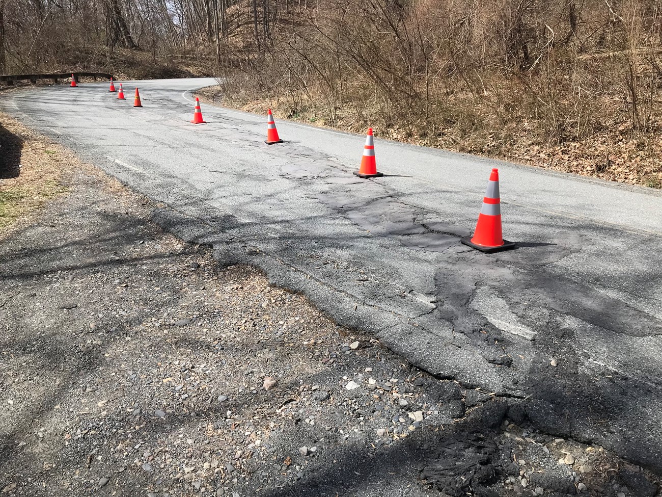 Bend in a road, with a crack that has been patched. Traffic cones warn that the road is becoming uneven.