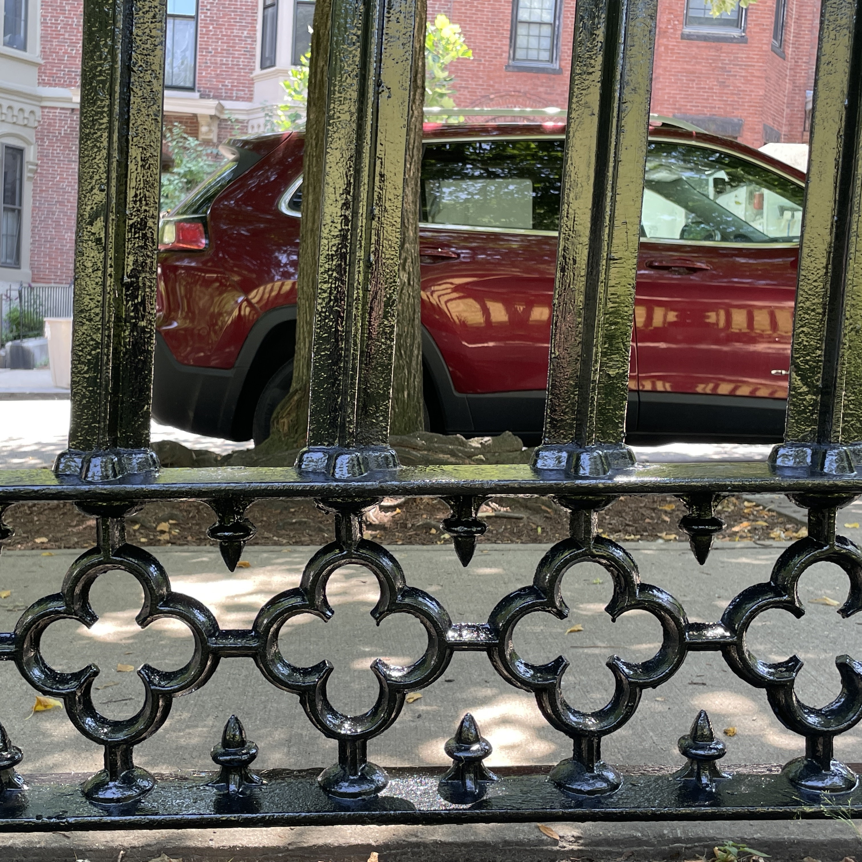 The bottom portion of a wrought-iron fence. Three bars and three floral decorations are visible. The fence is covered in lichen and the paint, formerly black, is now dark grey after weathering.