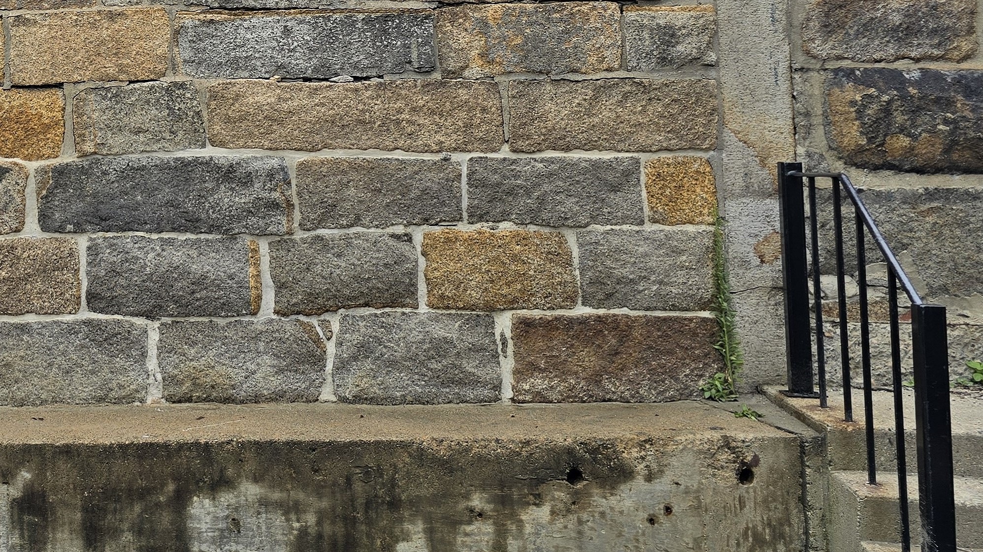 A closeup of a wall made from large, granite stone blocks. The mortar around the first two layers of blocks is newer and a brighter shade of grey than the mortar around the higher blocks.