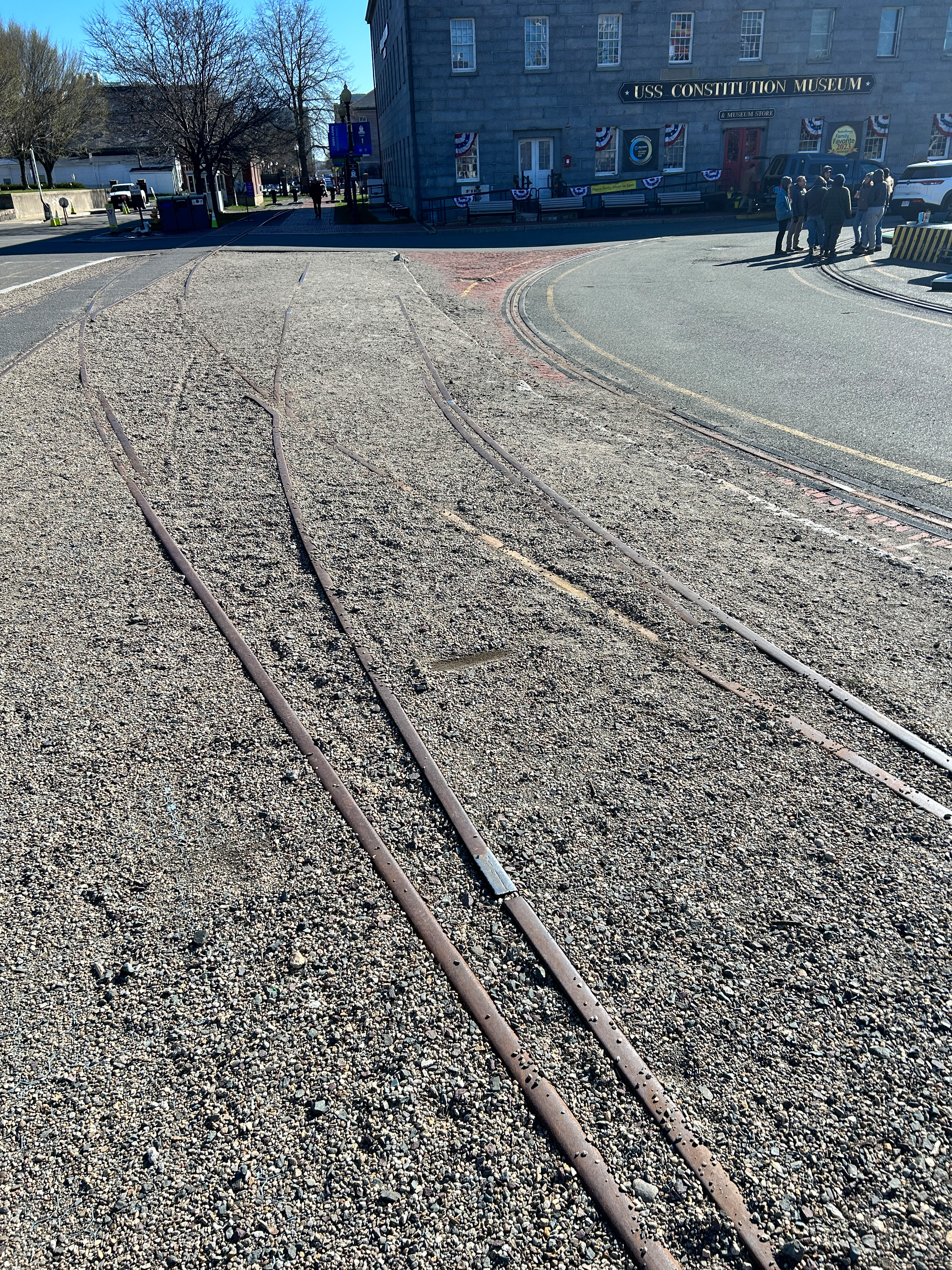 A trolley track diverts into two separate tracks. The ground inside and around the tracks is paved with gravel, much of which is spilling out onto the paved brick and asphalt outside the tracks.