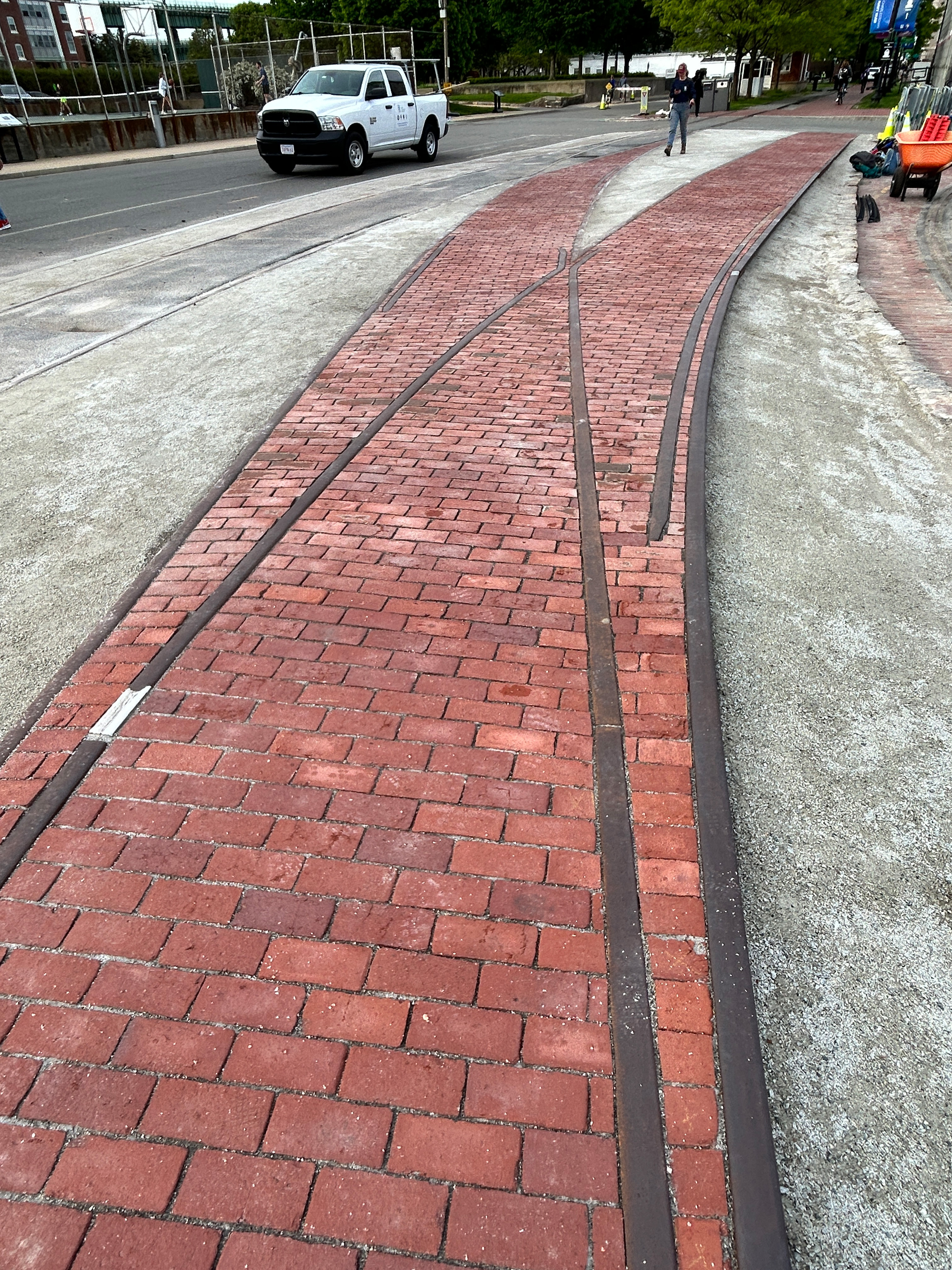 A trolley track diverts into two separate tracks. The ground inside and around the tracks is paved with gravel, much of which is spilling out onto the paved brick and asphalt outside the tracks.