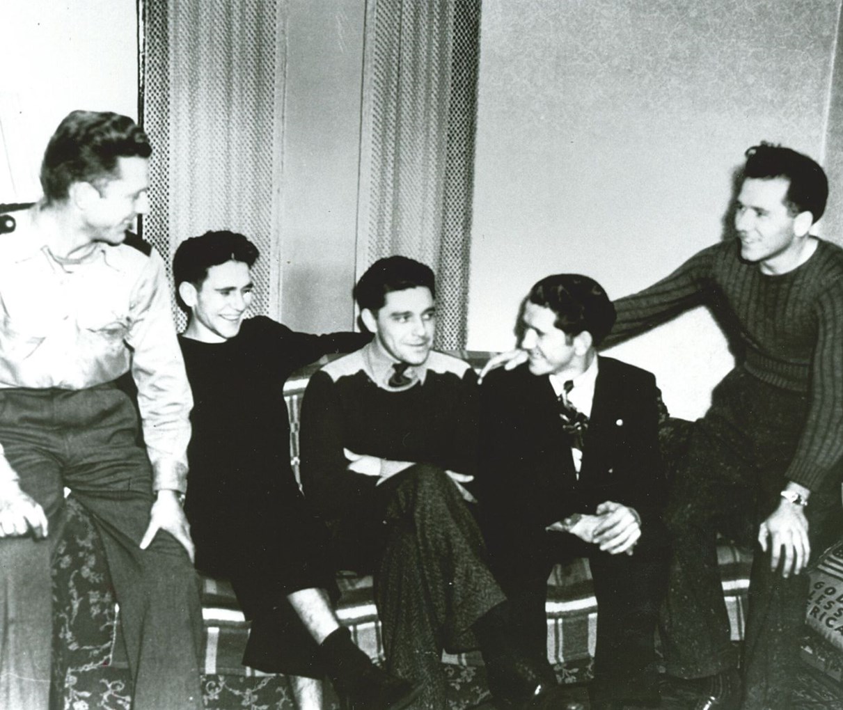 Black and white photo of four young men sitting on and around a couch