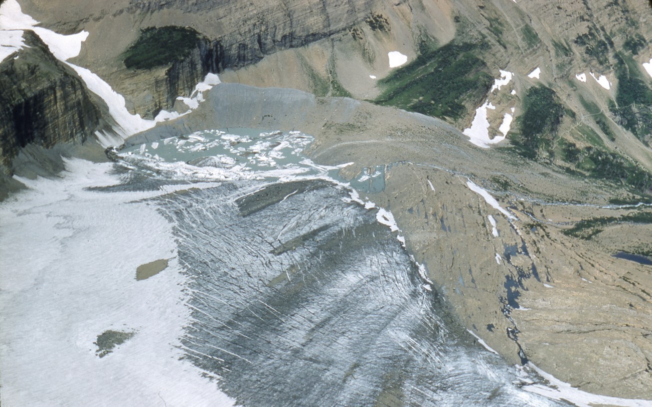 A grainy historic color photo of Grinnell Glacier from high above.