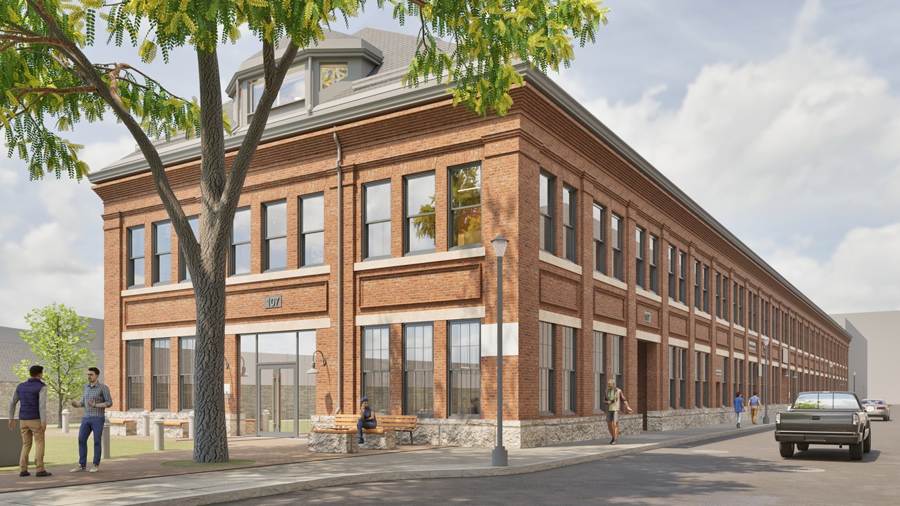 A long brick building that extends to the background. A tree in autumn sits before the building.