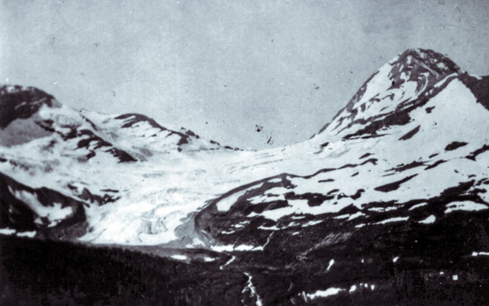 A fuzzy black and white landscape photograph of a glacier with a mountain on the right.