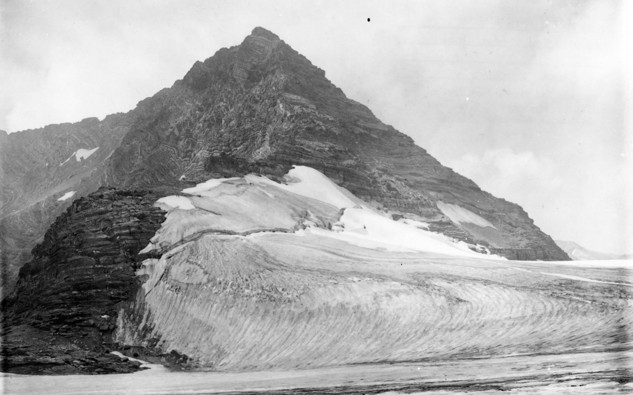 A pointed mountain with a ramp of snow on one side of it.