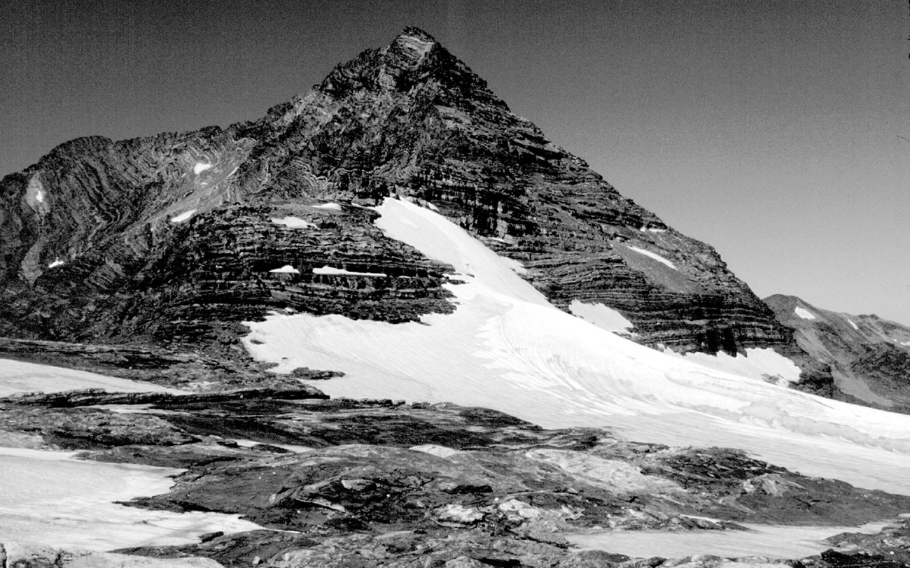 A pointed mountain with a ramp of snow on one side of it.