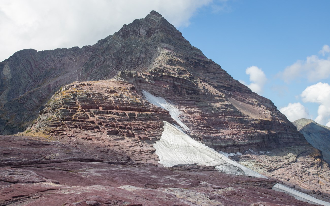 A pointed mountain with a ramp of snow on one side of it.