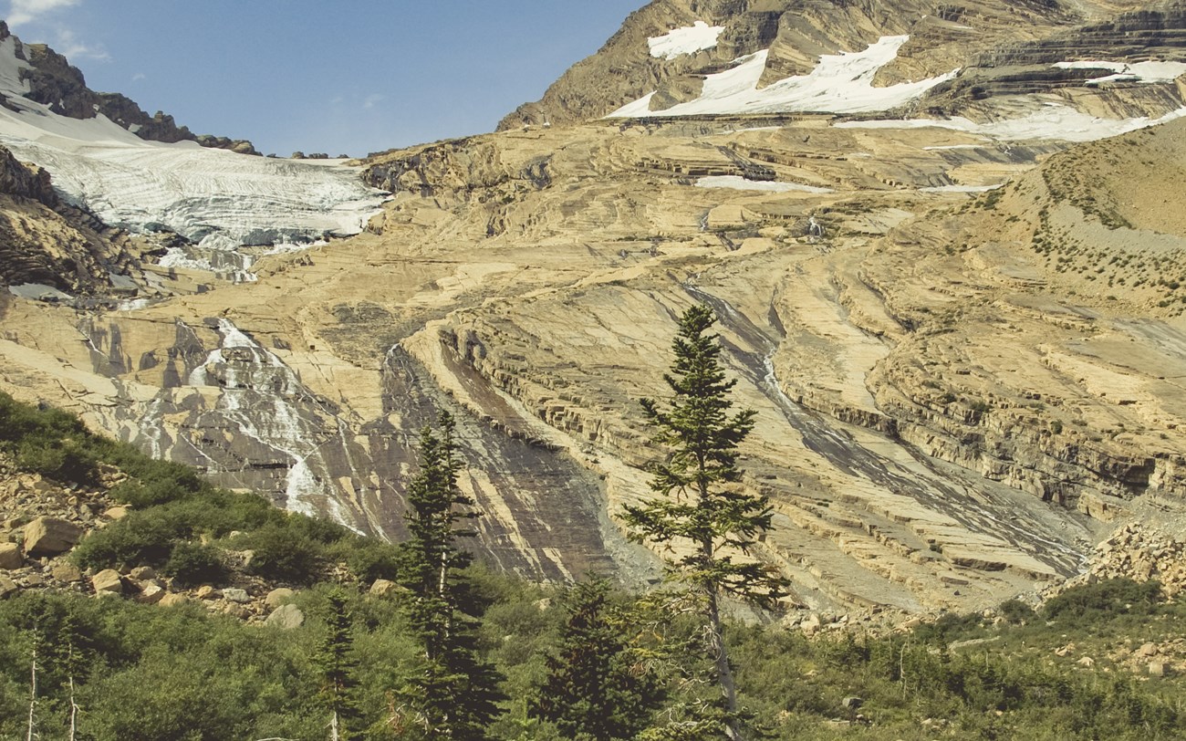 A landscape image of a glacier's footprint. Slabs of smooth rock with ice in the top corner.