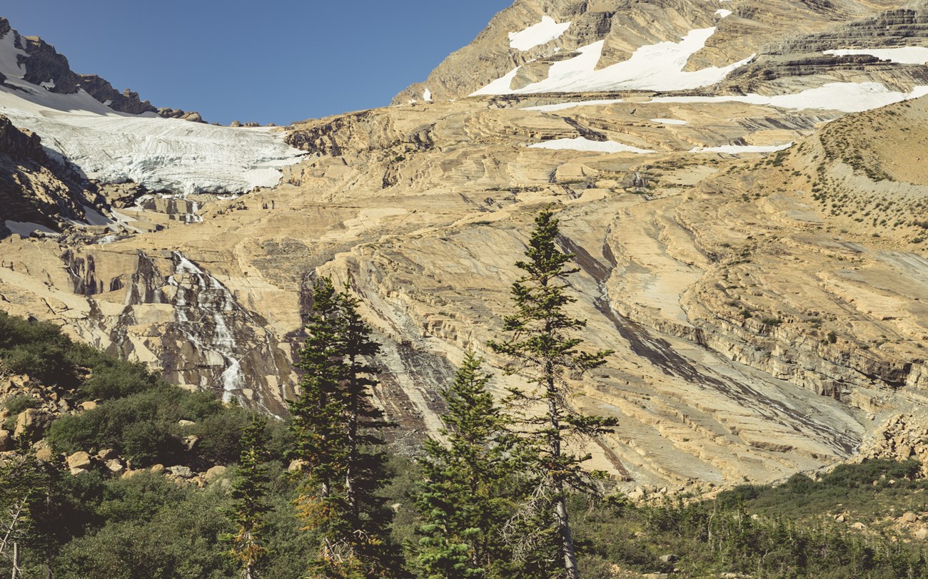 A landscape image of a glacier's footprint. Slabs of smooth rock with ice in the top corner.