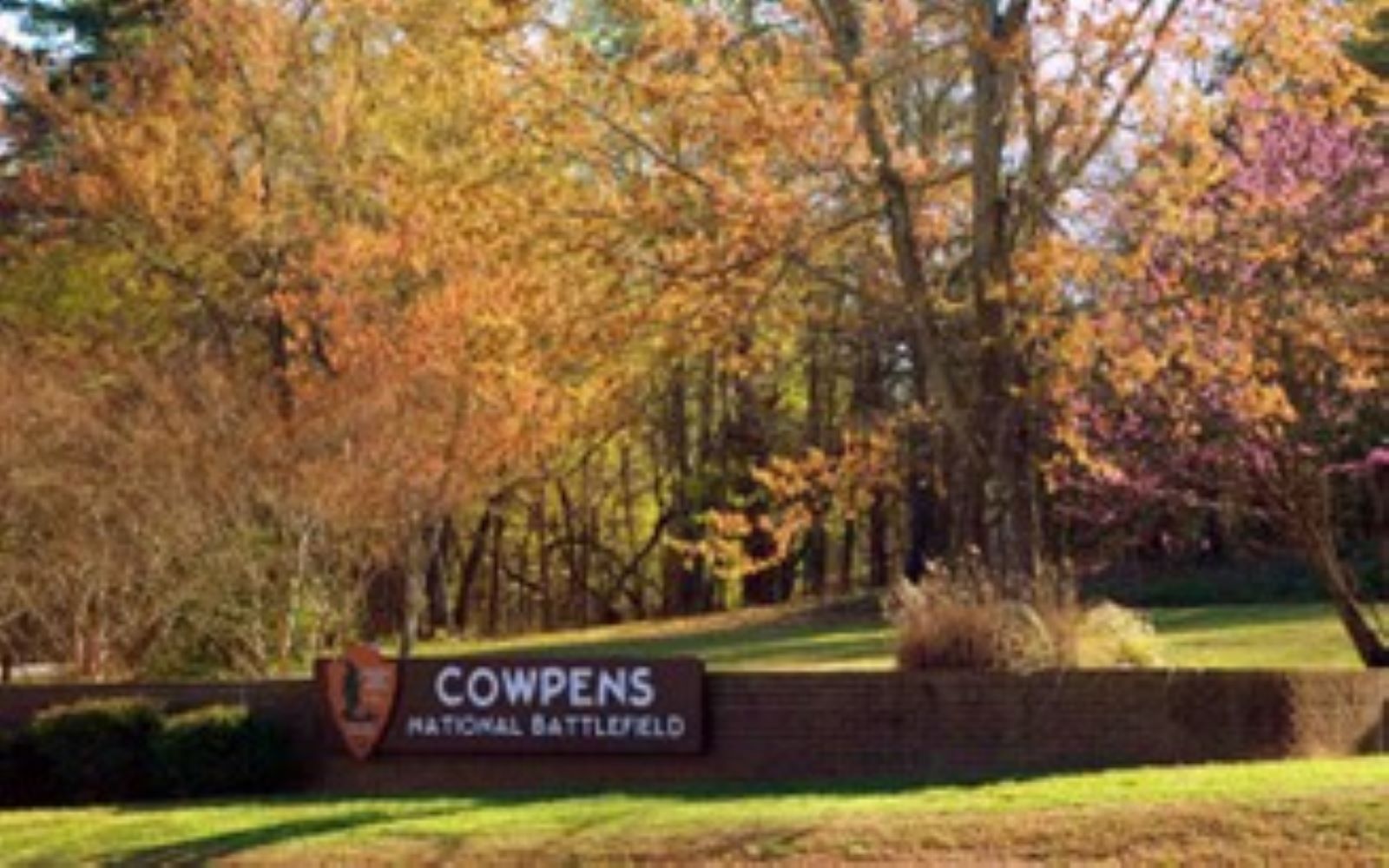 A National Park Service sign saying "Cowpens National Battlefield" with tress in the background.
