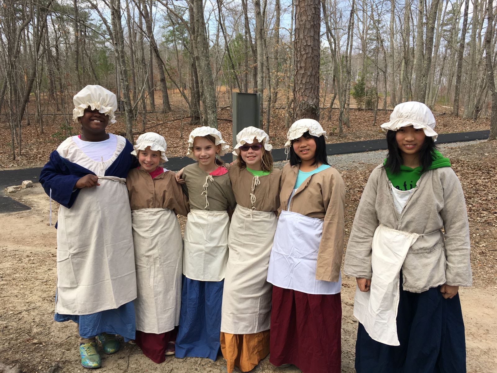6 smiling girls are wearing old timey clothes.