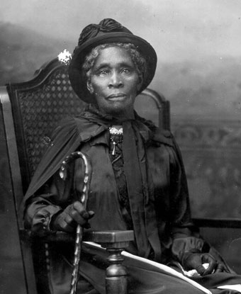 A woman sitting in a chair wearing a hat and holding a cane