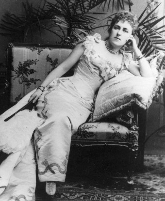 A woman wearing a gown, reclining on a sofa.