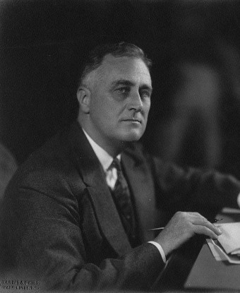 A man in a suite (FDR) seated at a desk in profile.