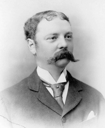 A head and shoulders portrait of a man with mustache wearing a suit.