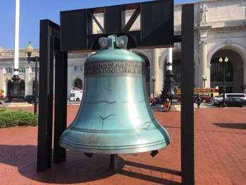 A bronze replica of the Liberty Bell sits on a red brick patio in front of Union Station