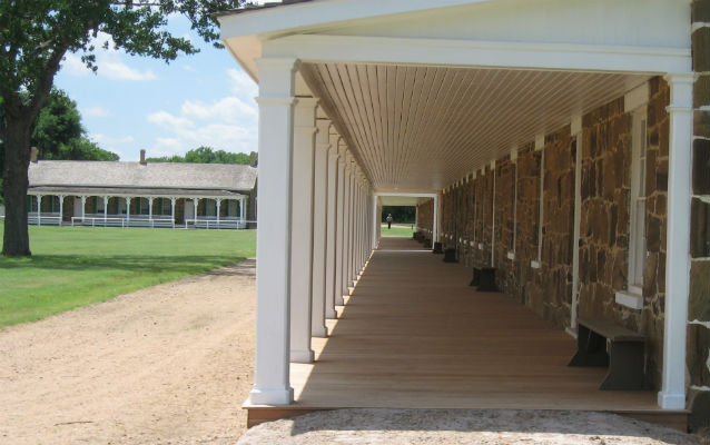 a dirt road passes in front of long stone building with white porch columns