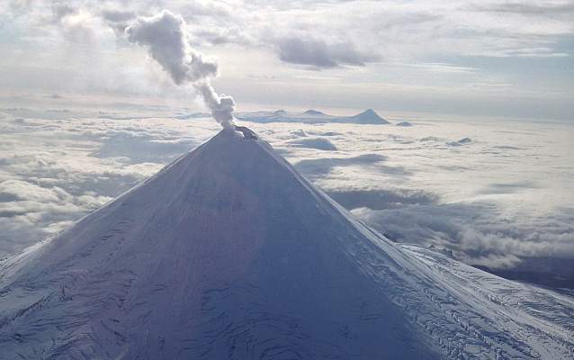 a snow covered volcano with smoke rising from the top