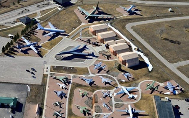 A collection of airplanes is groups around a former hanger building