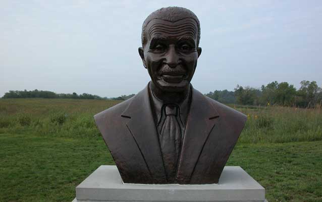 a bronze bust of George Washington Carver in front of green meadow