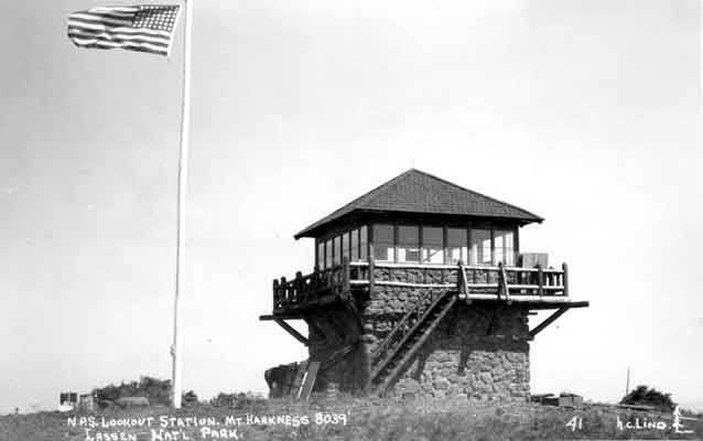 B&W; American flag flies above stone and wood fire tower
