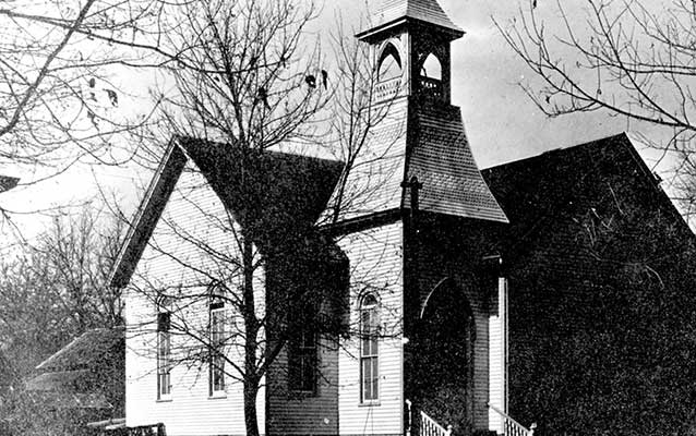 Black and white photograph of a white church with a steeple and gothic windows.