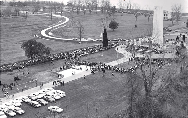 Large crowds of cars and people in foreground, houses of Fazendeville in background