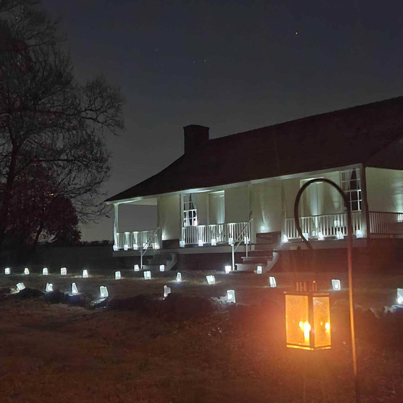 Luminary lanterns illuminate the front of the Ray House at night.