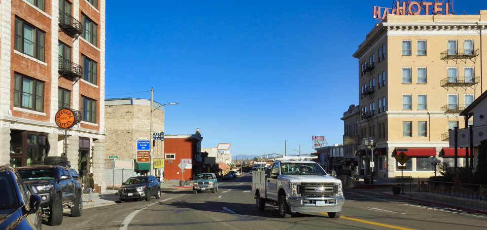 Painting of old race car with people, buildings, and banner.
