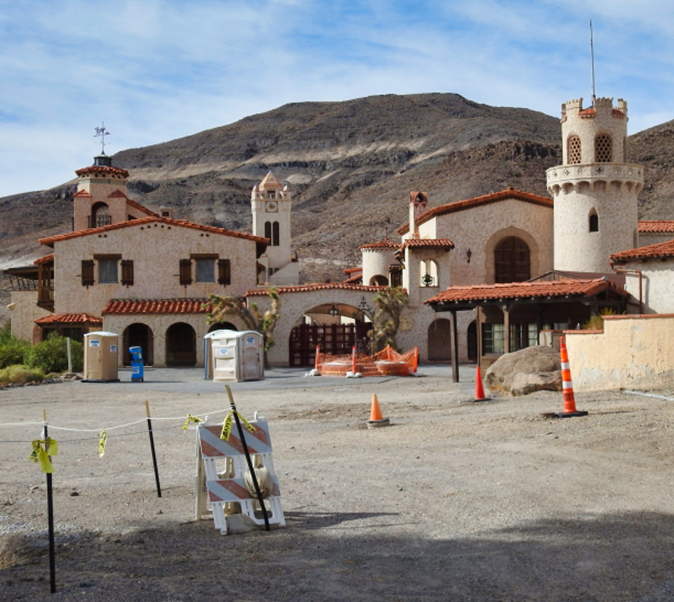 Man and woman walking with Spanish-style buildings behind them.