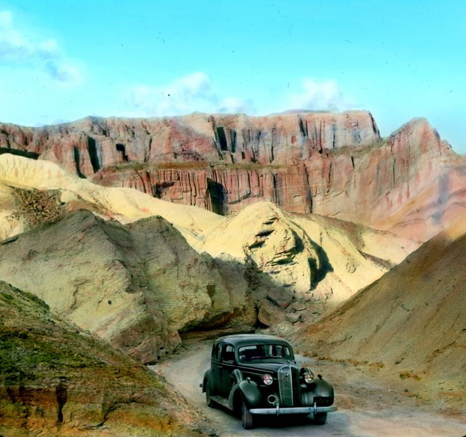 Car drives through narrow road with cliffs in background