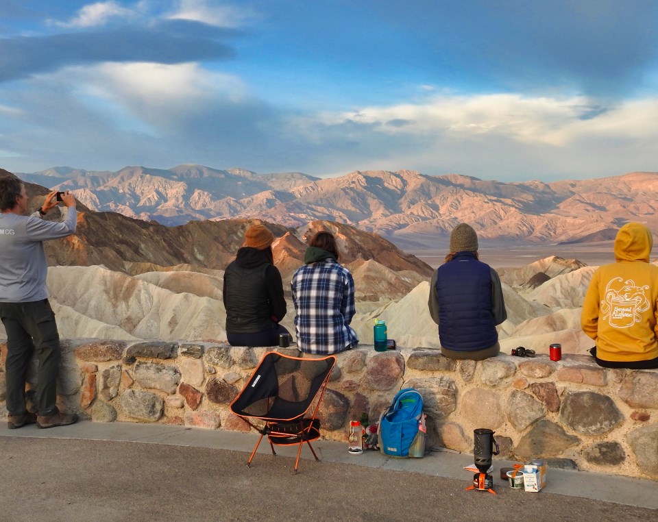 Old car with people parked overlooking desert landscape.