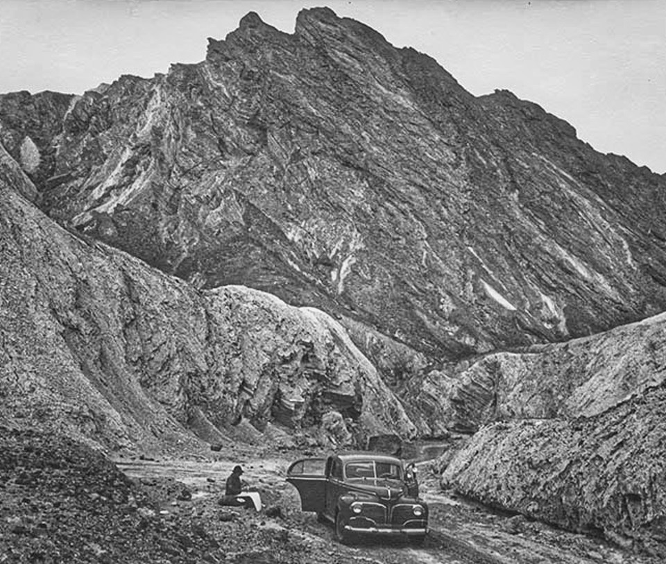 Person sitting next to car drawing with rocky cliffs in background.