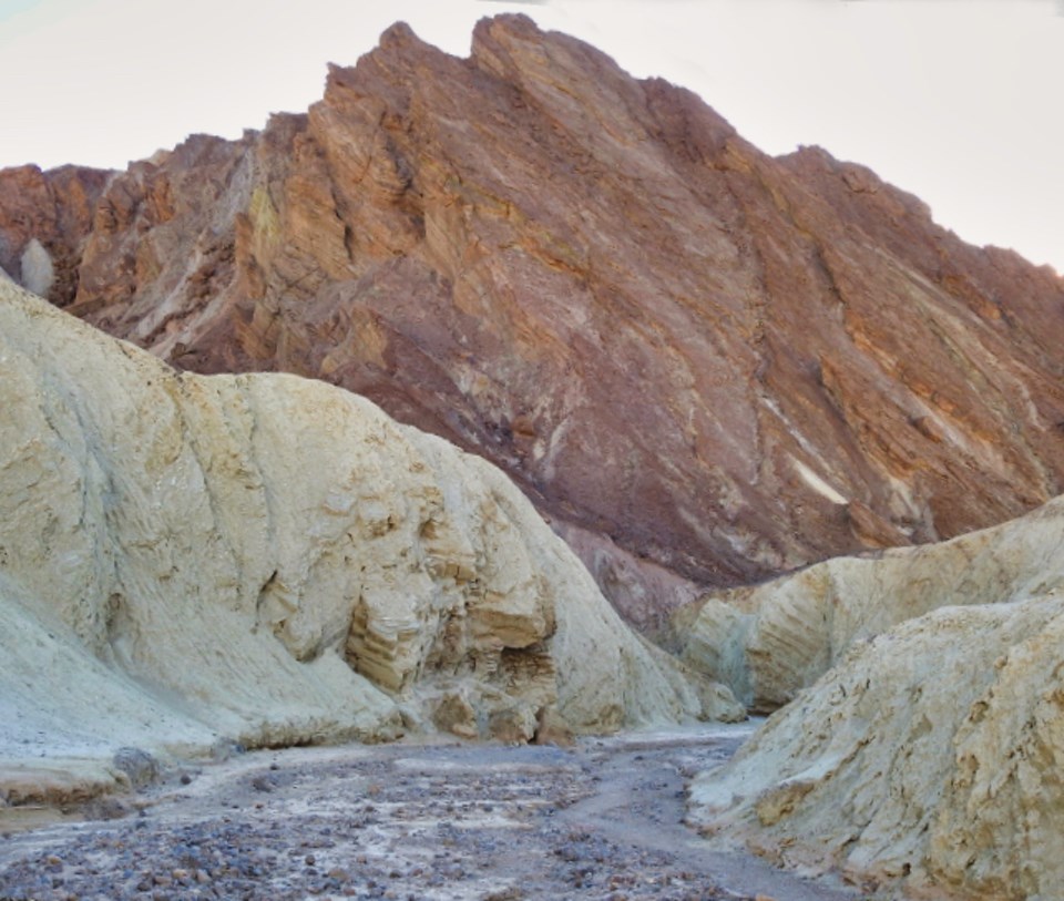 Person sitting next to car drawing with rocky cliffs in background.