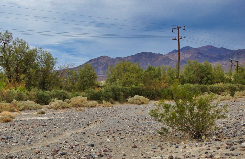 Children stand in front of straw huts with mountains in background.