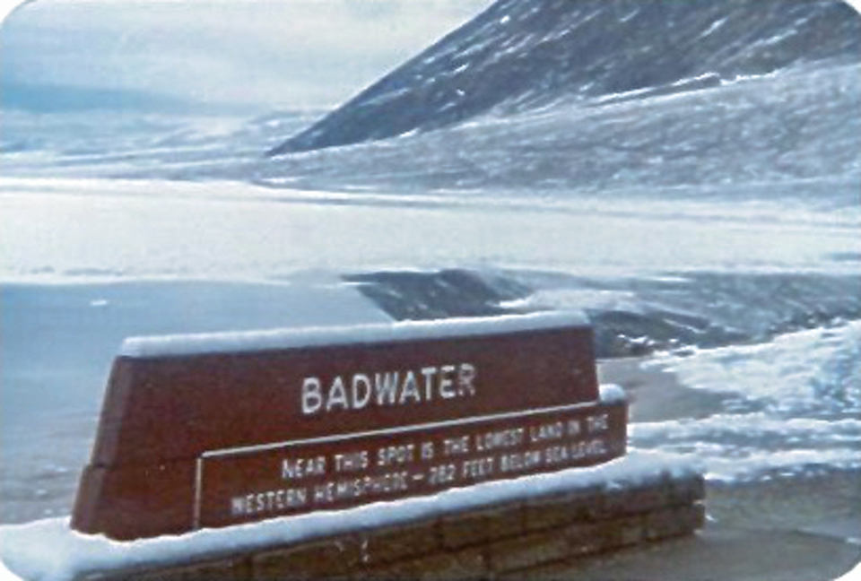 Sign with pool and hillside behind covered in snow.