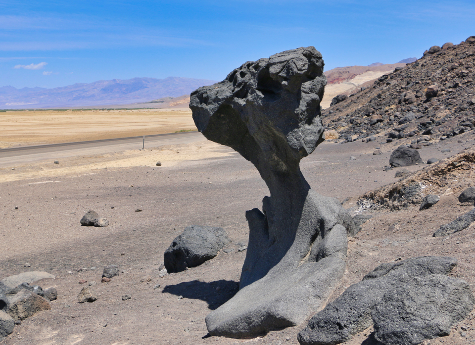 A large rock outcropping shaped like a mushroom next to a road.