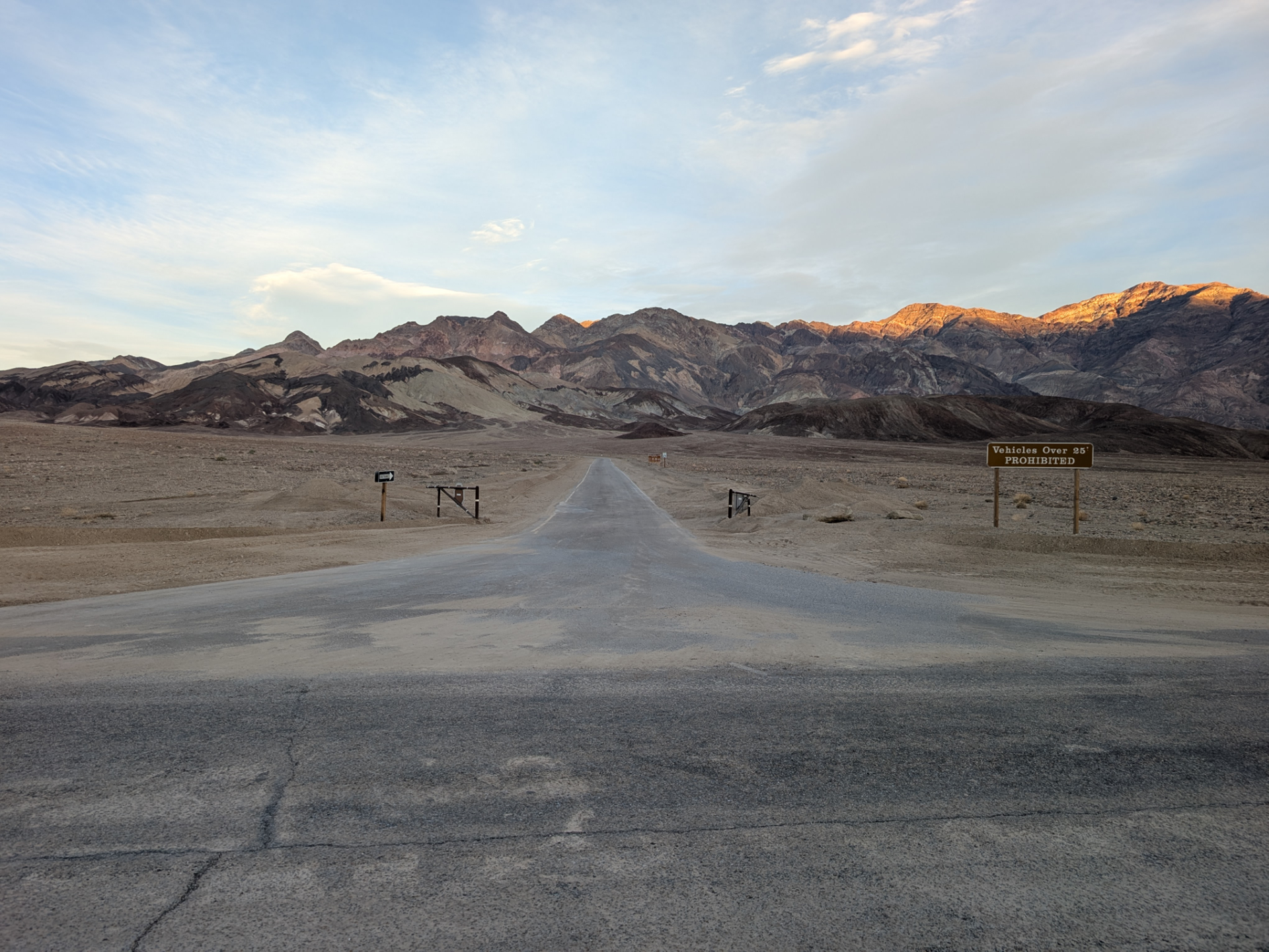 Brown dirt and rocks cover the landscape with distant bare mountains. Only signs and gates show that there was a road here.