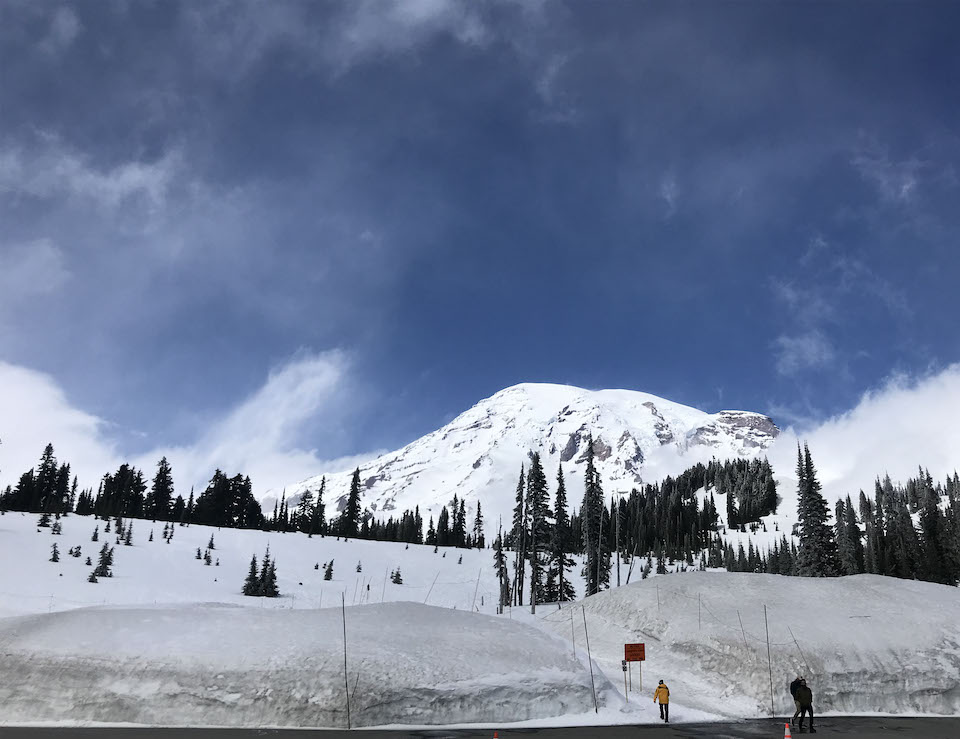 Profundos bancos de nieve rodean a una zona de estacionamiento, con los alrededores completamente ocultos por la niebla y nubes bajas.