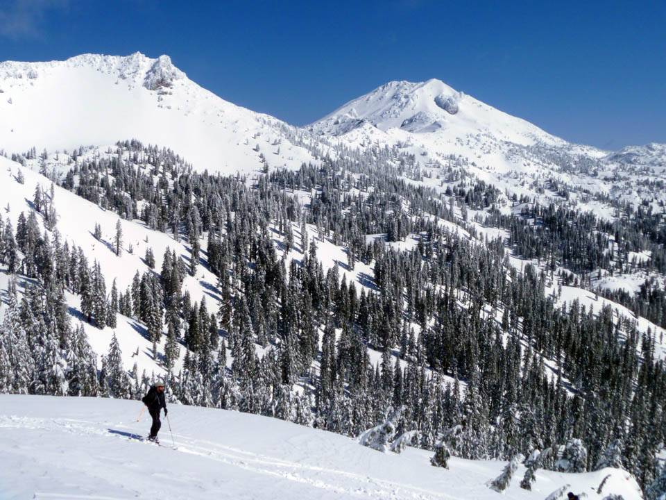 A landscape photo of a skier below two snow-covered volcanic peaks.