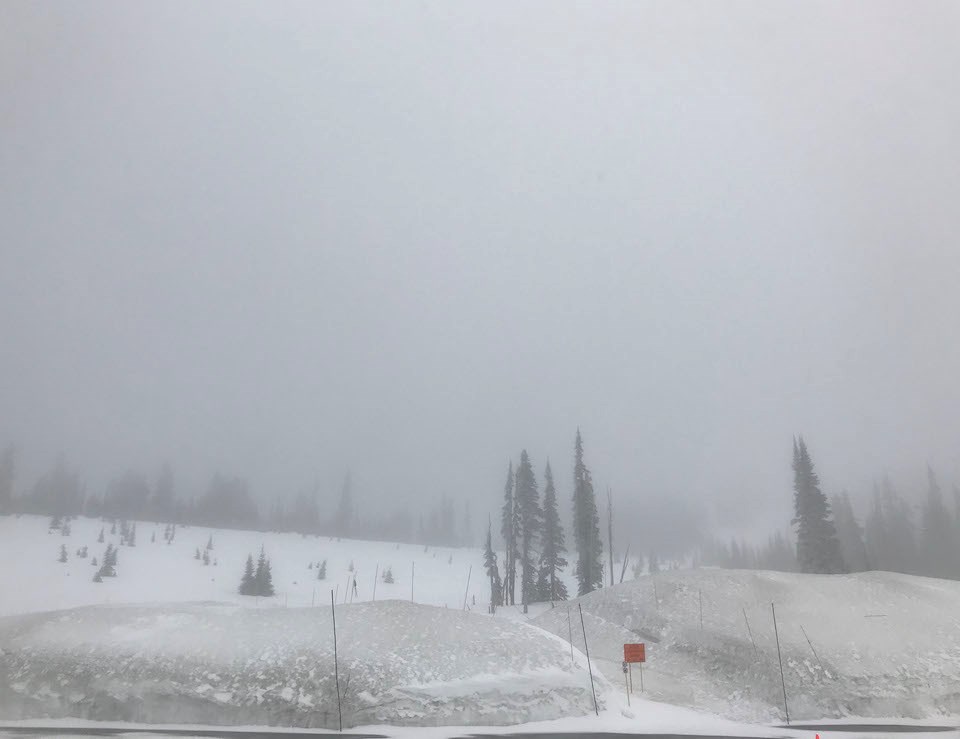 Deep snowbanks surround a parking lot with the view completely obscured by low fog and clouds.