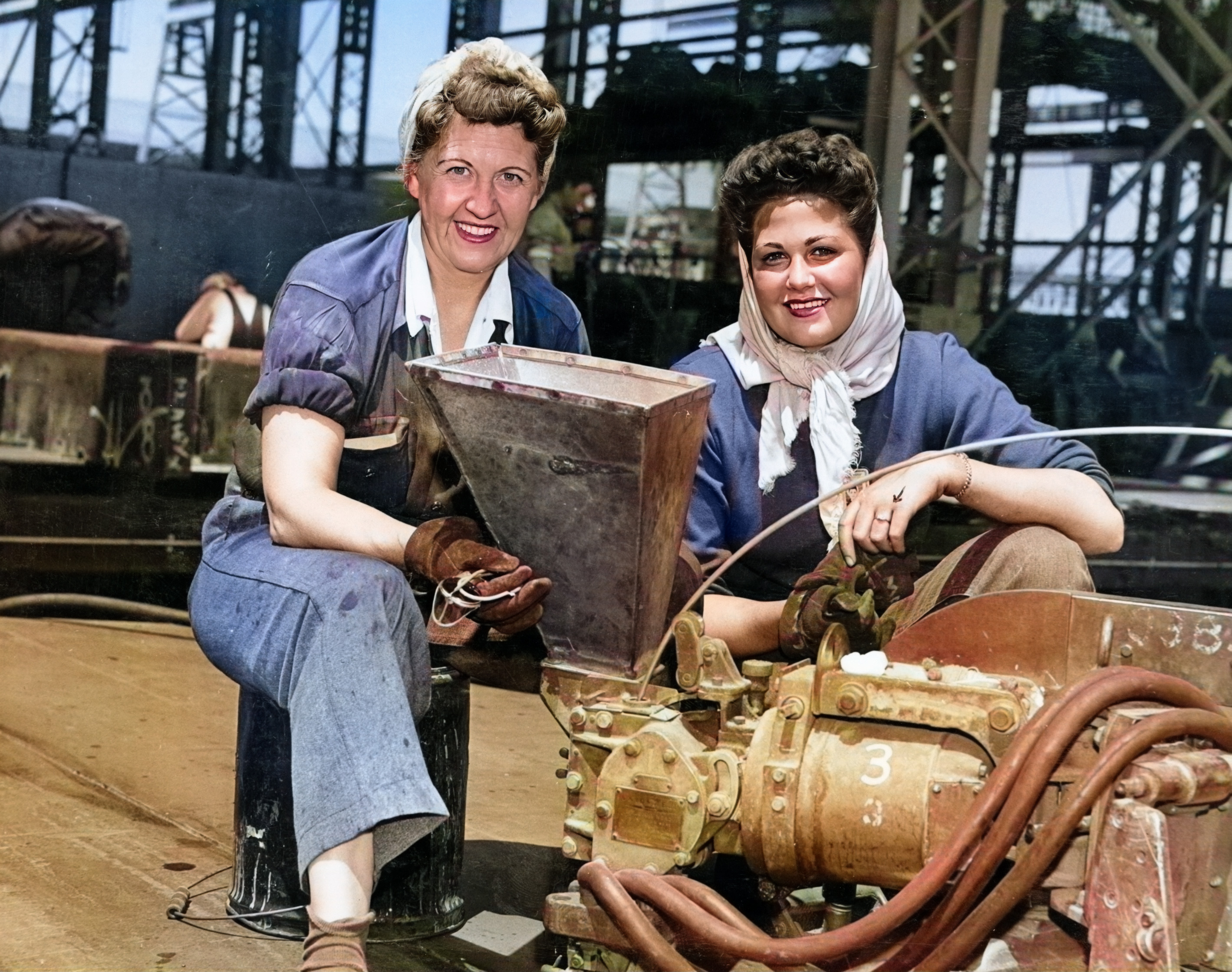 Historic photo of two women shipyard workers smiling at the camera. Industrial machines and equipment.