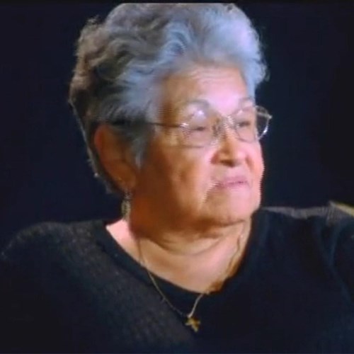 An Alaska Native woman with gray, coiffed hair wears glasses and looks to her side.