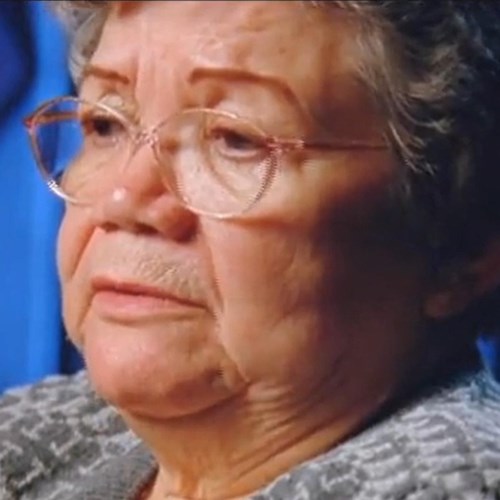 an Alaska Native woman with gray, curly hair wears a sweater and glasses.