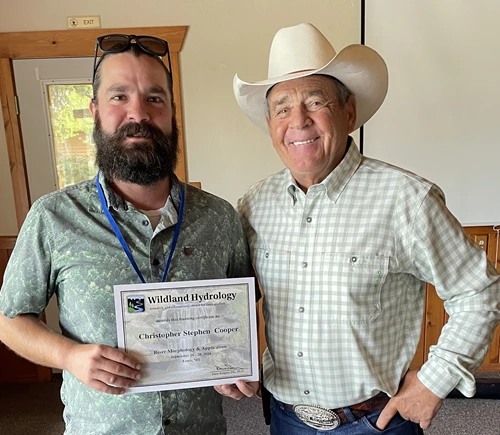 Man in beard holding a certificate standing next to man in cowboy hat