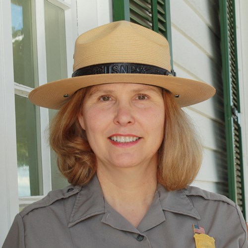 A white woman with blonde hair wearing a National Park Service uniform smiles at the camera.