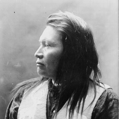 Black and white photograph of a Native American man with long hair, wearing a beaded vest.