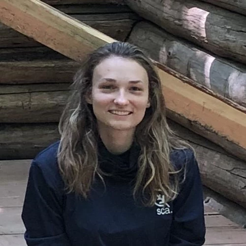 A young adult wearing a uniform sits on a log wooden structure in the forest